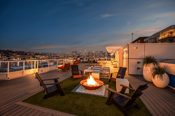 A rooftop patio with a fire pit and chairs overlooking a city skyline at dusk. at The Summit at Lake Union, Seattle, Washington